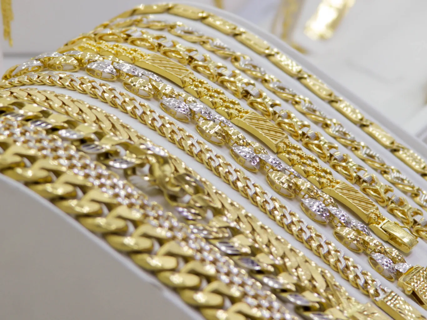 At the intake stage, a worker lays several gold chains in measured loops on a dark tray and uses a small jewelry ruler to check their lengths before recording the details