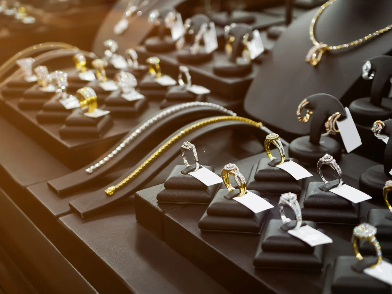 A worker uses a jeweler's touchstone and testing solution during the verification stage of a new gold jewelry evaluation, with a necklace and ring resting in an open presentation box nearby
