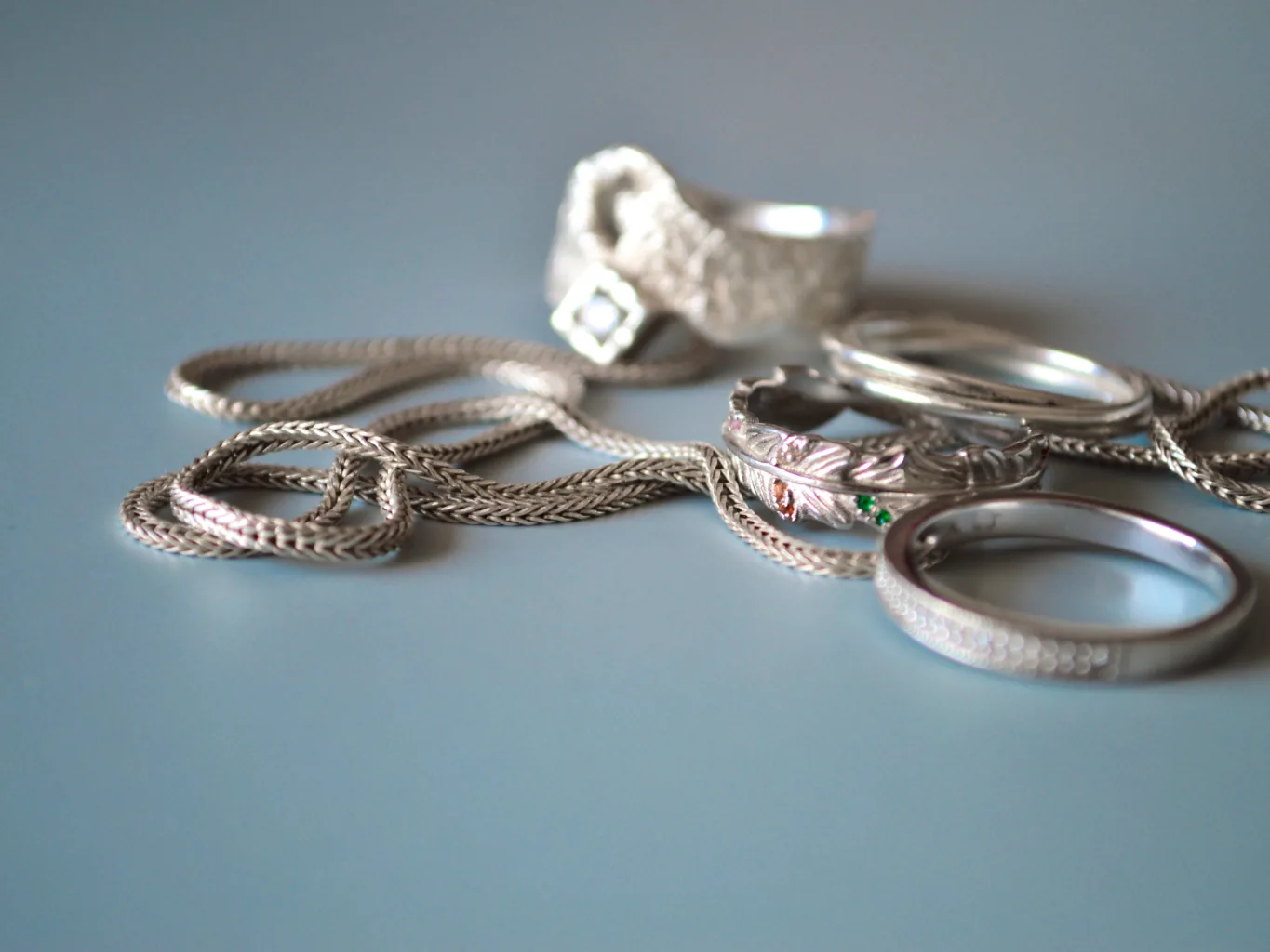 A worker uses a soft jewelry polishing cloth during the preparation stage of a silver jewelry evaluation, carefully wiping a pair of earrings beside a necklace and bracelet on a dark counter